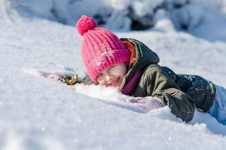 Jente ligger på snøen og smiler