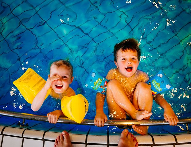 To søsken bader i basseng og smiler opp til kamera