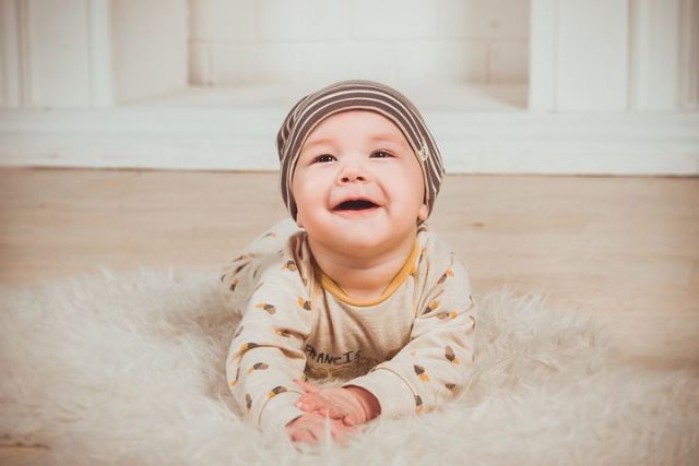 Baby ligger på teppegulv og smiler stort