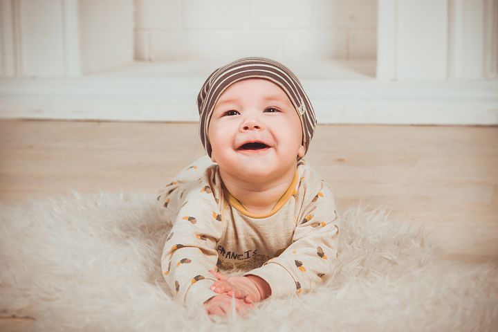 Baby ligger på teppegulv og smiler stort