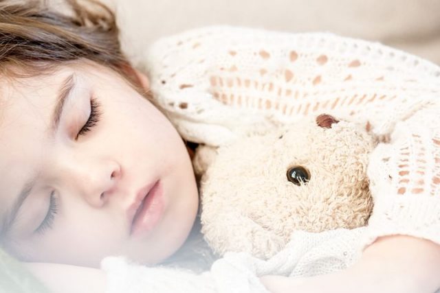 En liten jente sover med bamsen sin